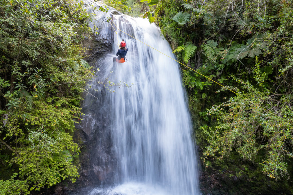 Canyoning en el Rio Correntoso de Pucón. Turista rapeleando la cascada con cuerda.